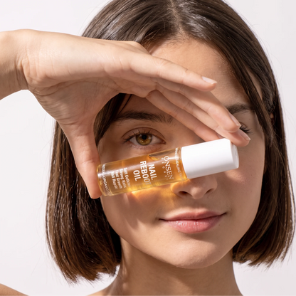 Onsen Secret nail reboot oil promotional image, clear bottle with golden liquid held in front of face emphasizing natural nail care benefits.