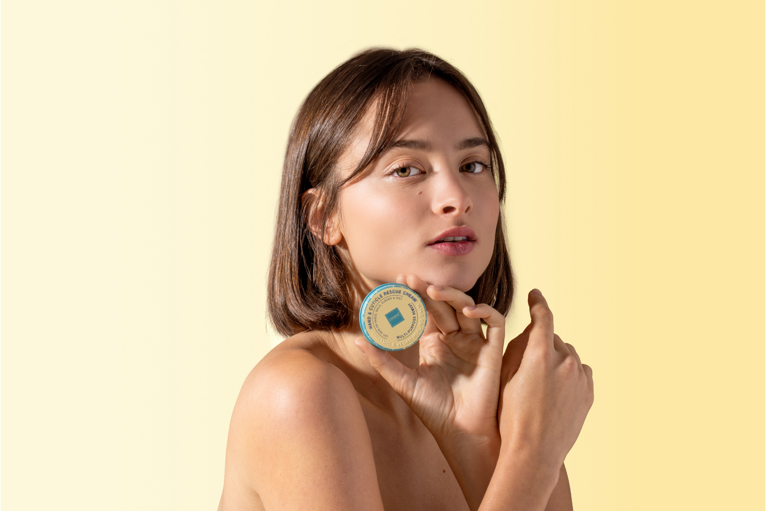 Woman holding a hand and cuticle rescue cream against a yellow background