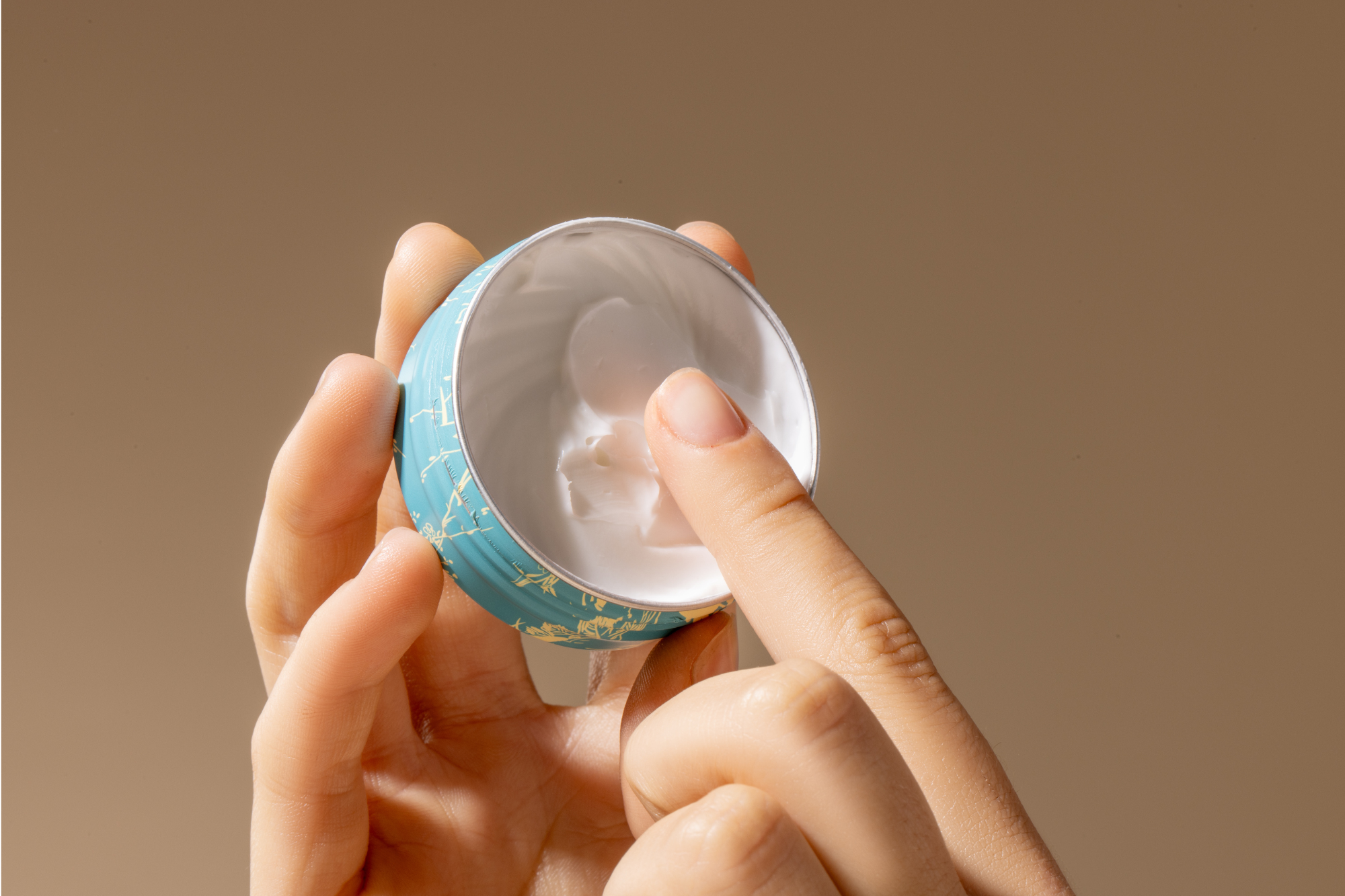 Hand holding a hand and cuticle rescue cream with a beige background