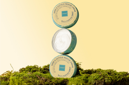 Three containers of hand and cuticle rescue cream on a grassy background