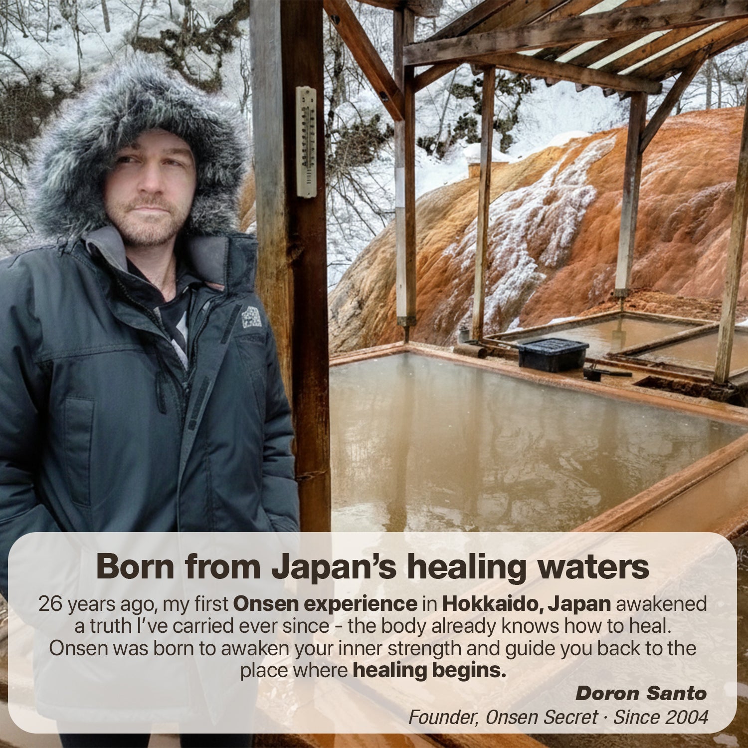Man in a winter coat standing next to a wooden structure with snow-covered ground and trees in the background.